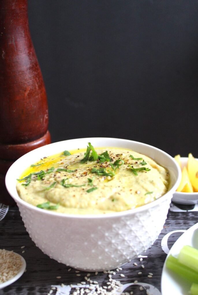 A hummus served in a bowl. Texture is creamy and smooth. Some sesame seeds on the table.